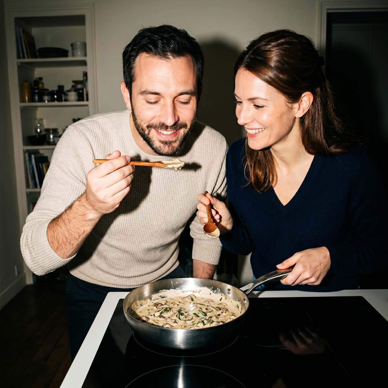 Couple souriant qui déguste ensemble des pâtes aux champignons dans une poêle inox 22 cm SAINE sur une plaque de cuisson à induction