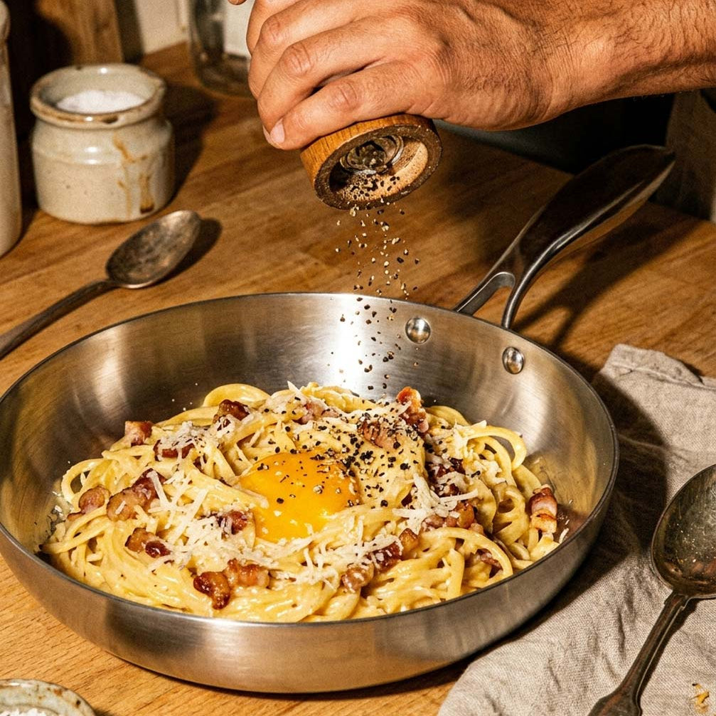 Carbonara crémeuse avec un jaune d'oeuf et du parmesan dans une poêle inox 26 cm SAINE, une main moud du poivre par-dessus, style vintage