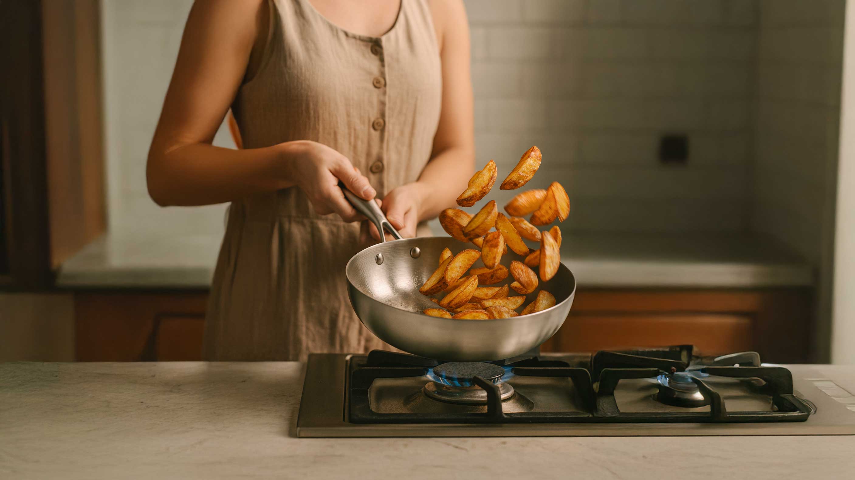 une femme fait cuire des pommes de terre sautées dans une poêle en inox SAINE