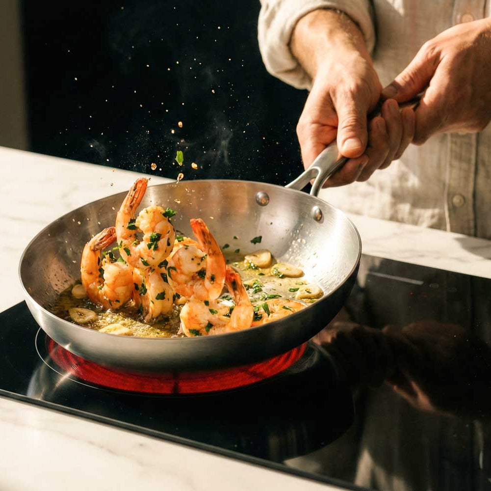 des crevettes cuisent dans une poele inox sur des plaques à induction