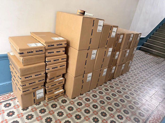 Cartons SAINE de poêles et casseroles inox stockés au pied d'un escalier avant expédition