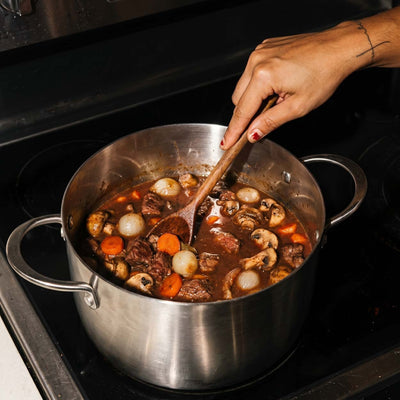 Bœuf bourguignon qui mijote dans une marmite inox SAINE avec champignons, carottes et oignons, remuant avec une spatule en bois