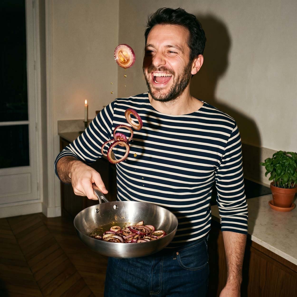 Homme souriant qui fait sauter des rondelles d'oignons rouges au-dessus d'une poêle inox 24 cm SAINE dans sa cuisine