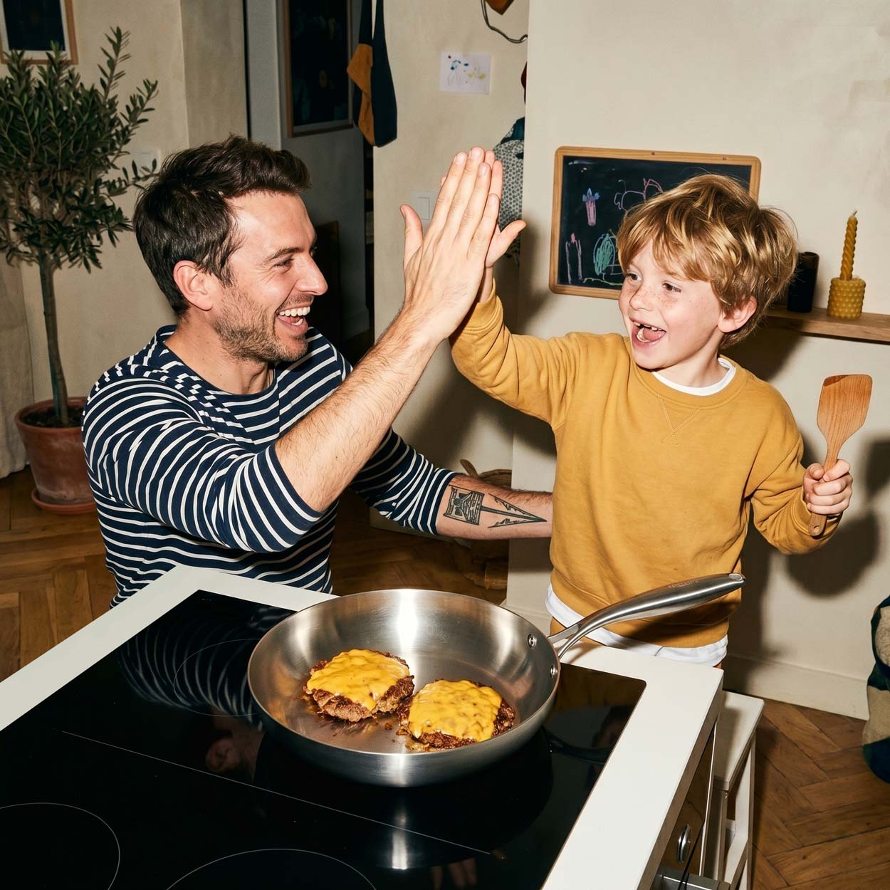 Père et fils qui se font un high-five joyeux après avoir préparé des burgers au fromage dans une poêle inox 24 cm SAINE sur une plaque à induction
