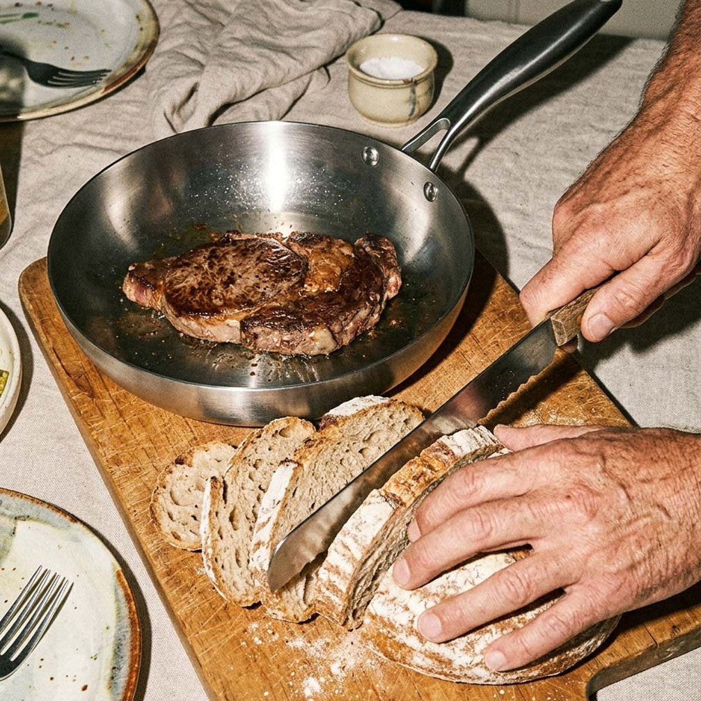 Steak doré dans une poêle inox 22 cm SAINE posée sur une table rustique, à côté d'un pain artisanal tranché, style vintage