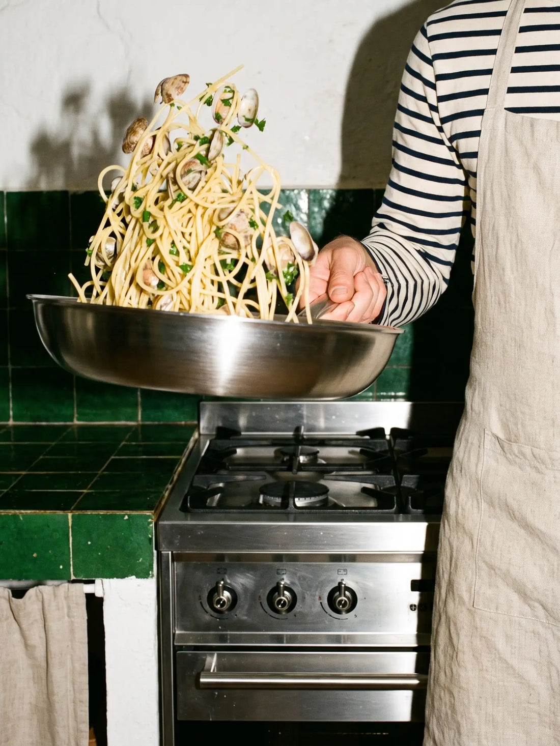 Spaghetti aux palourdes sautés dans la poêle inox 32 cm SAINE au-dessus d'une cuisinière gaz