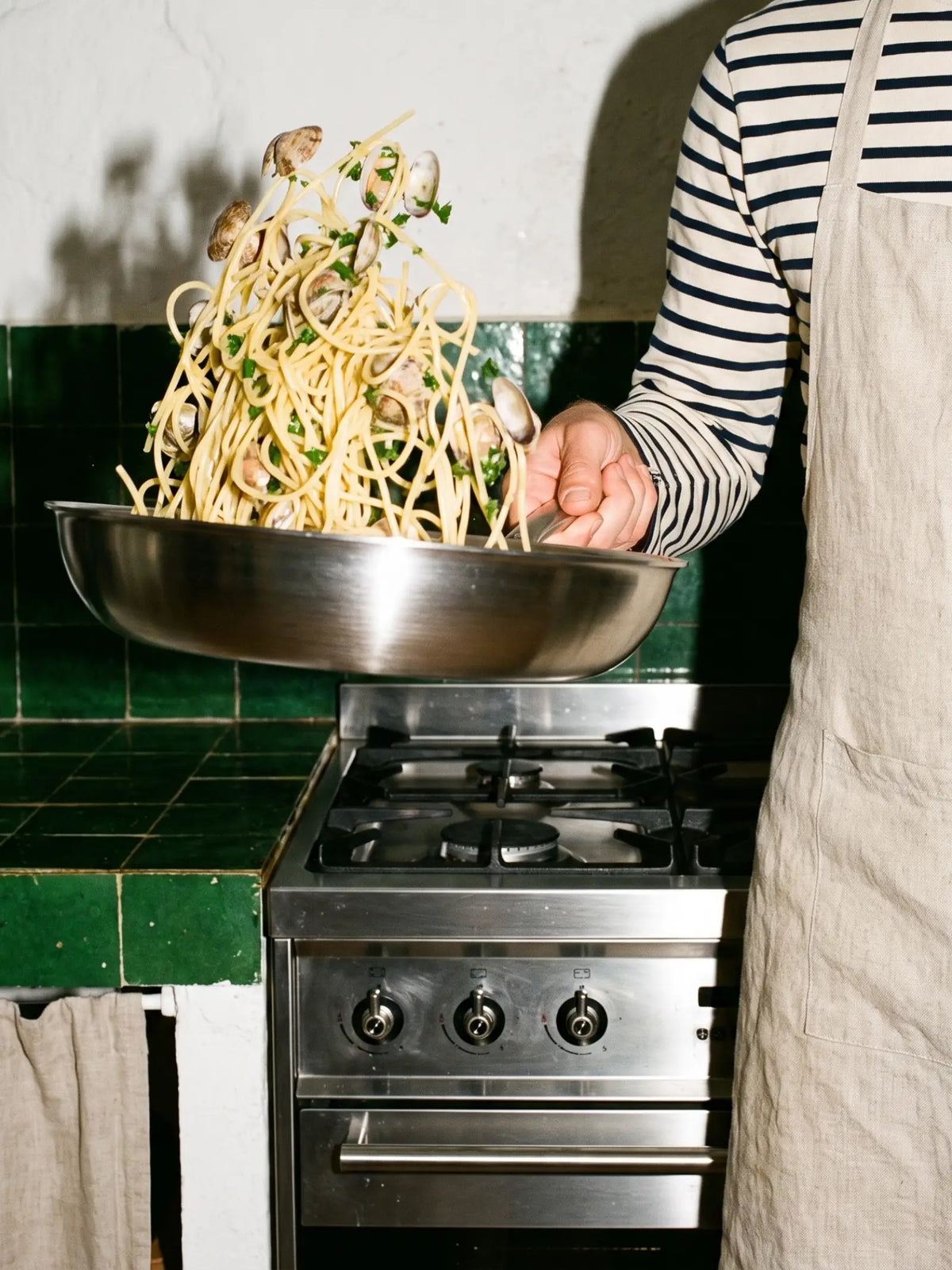 Spaghetti aux palourdes sautés dans la poêle inox 32 cm SAINE au-dessus d'une cuisinière gaz